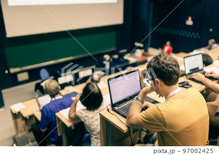 Workshop at university. Rear view of students sitting and listening in lecture hall doing practical tasks on their laptops. 97002425