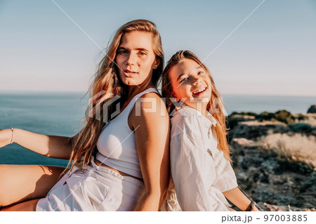 Sea family vacation together, happy mom and teenage daughter hugging and smiling together over sunset sea view. Beautiful woman with long hair relaxing with her child. Concept of happy friendly family 97003885