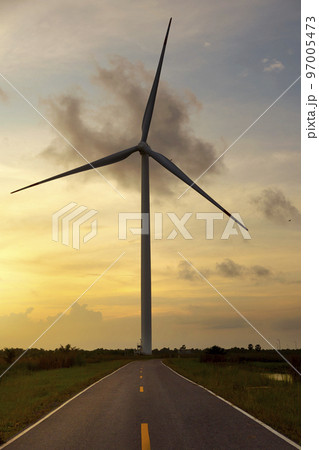 Wind turbine standing by the road against a sunset sky and a green meadow. Wind turbine standing by the road against a sunset sky and a green meadow. 97005473