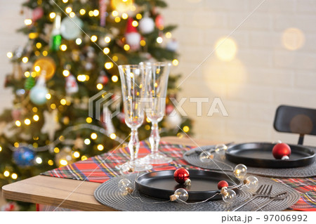 Festive table set in the living room for Christmas and New year in loft style. Christmas tree, black plates and forks, woven napkins, trendy tableware, cozy interior of the house 97006992