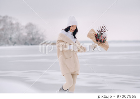 A girl in a beige cardigan and winter flowers walks in nature in the snowy season. Winter weather 97007968