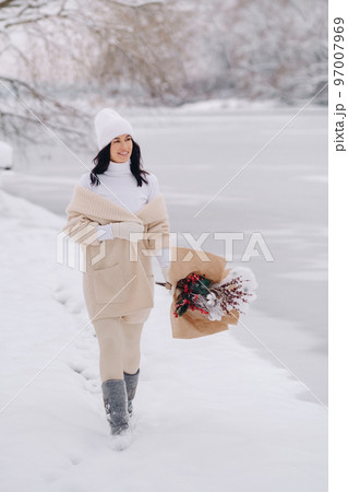 A girl in a beige cardigan and winter flowers walks in nature in the snowy season. Winter weather A girl in a beige cardigan and winter flowers walks in nature in the snowy season. Winter weather 97007969