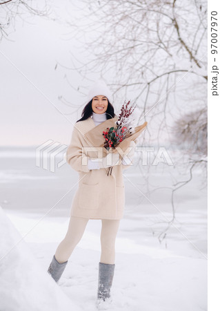 A girl in a beige cardigan and winter flowers walks in nature in the snowy season. Winter weather A girl in a beige cardigan and winter flowers walks in nature in the snowy season. Winter weather 97007970