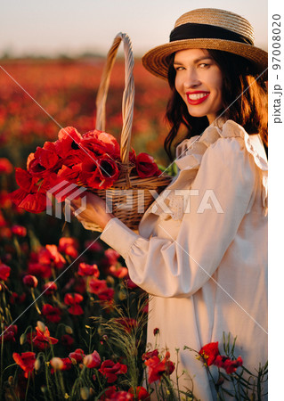 A girl in a white dress and with a basket of poppies walks through a poppy field A girl in a white dress and with a basket of poppies walks through a poppy field 97008020
