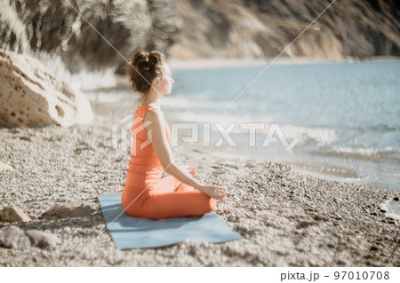 Woman sea yoga. Selective focus. Young beautiful caucasian woman in a red suit practicing yoga on the beach at sunrise near the sea. Yoga. Healthy lifestyle. Meditation concept. Woman sea yoga. Selective focus. Young beautiful caucasian woman in a red suit practicing yoga on the beach at sunrise near the sea. Yoga. Healthy lifestyle. Meditation concept. 97010708