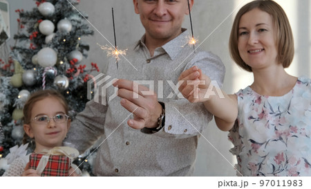 Family of three holding sparklers while celebrating Xmas or New year at home, selective focus Family of three holding sparklers while celebrating Xmas or New year at home, selective focus 97011983