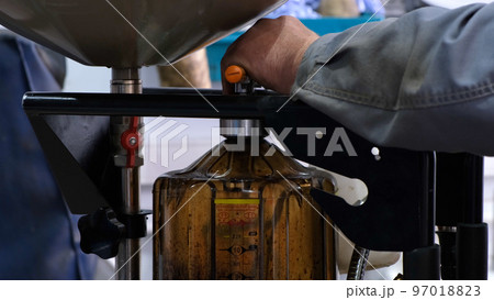 Change engine oil. The male hands of a mechanic drain the old oil from the car into a special container. Old dirty oil being drained from underneath a car during an oil change 97018823