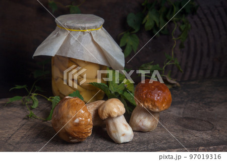 Porcini mushroom commonly known as Boletus Edulis and glass jar with canned mushrooms on vintage wooden background.. Porcini mushroom commonly known as Boletus Edulis and glass jar with canned mushrooms on vintage wooden background.. 97019316