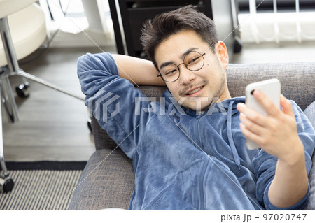 ソファーで寝ながらスマートフォンを使う男性 97020747