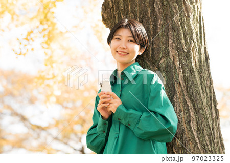 木に寄りかかってスマホを操作する女性 97023325