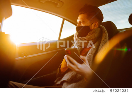 Young man in protective sterile mask in taxi car on a back seat checking her cell phone. 97024085