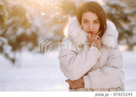 Beautiful woman in winter clothes posing in a snowy park. Young lady walking in a sunny winter day. Beautiful woman in winter clothes posing in a snowy park. Young lady walking in a sunny winter day. 97025245