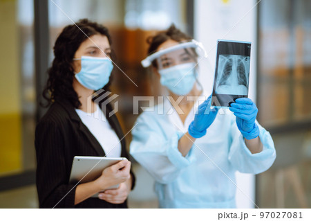 A female doctor in visor and protective gloves discussing an x-ray. Doctor examines an X-ray. A female doctor in visor and protective gloves discussing an x-ray. Doctor examines an X-ray. 97027081