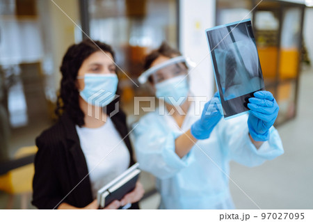 A female doctor in visor and protective gloves discussing an x-ray. Doctor examines an X-ray. 97027095
