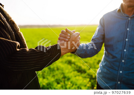 Handshake two farmer on the background of a wheat field at sunset. The concept of the agricultural business. Handshake two farmer on the background of a wheat field at sunset. The concept of the agricultural business. 97027639