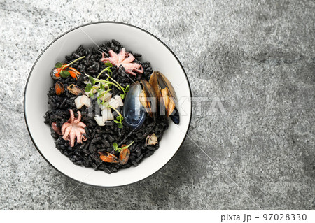 Delicious black risotto with seafood in bowl on light grey table, top view. Space for text Delicious black risotto with seafood in bowl on light grey table, top view. Space for text 97028330