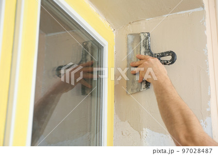 Man plastering window area with putty knife indoors, closeup. Interior repair 97028487