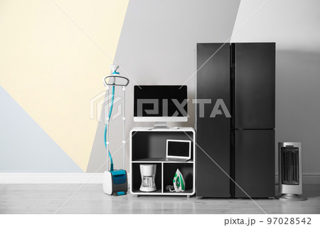 Modern refrigerator and other household appliances near color wall indoors Modern refrigerator and other household appliances near color wall indoors 97028542