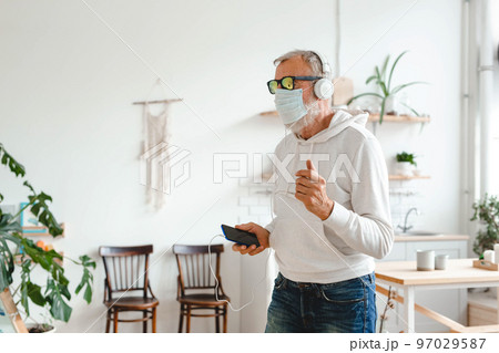Senior man with medical mask on face dance and using smartphone app for creating playlist music on mobile app copy space - Elderly male having fun dancing with mobile phone technology - Tech and Senior man with medical mask on face dance and using smartphone app for creating playlist music on mobile app copy space - Elderly male having fun dancing with mobile phone technology - Tech and 97029587