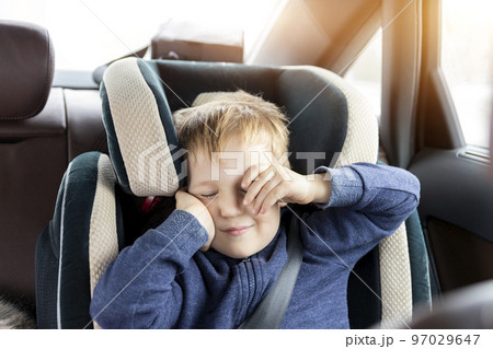 Cute caucasian toddler boy awaken and rub eyes in child safety seat in car during road trip. Adorable baby dreaming asleep comfortable chair during journey in vehicle. Children care safety on roads 97029647