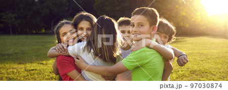 Group of happy little children hugging each other while having fun in sunny summer park 97030874
