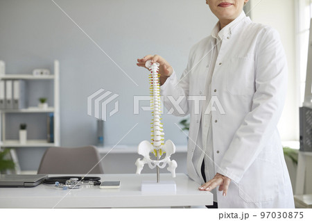 Cropped shot of orthopedic surgeon standing by table with anatomical model of human spine 97030875