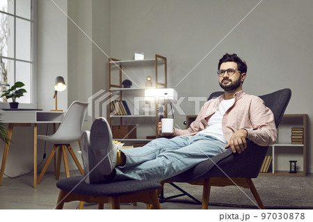 Relaxed man sitting in an armchair at home, using a projector, watching a movie, drinking coffee 97030878