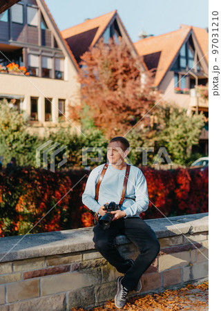 Man Sitting in Old European City And Holding Photo Camera. Contemporary Stylish Blogger And Photographer. Handsome man taking a selfie on a trip in Europe. Man Sitting in Old European City And Holding Photo Camera. Contemporary Stylish Blogger And Photographer. Handsome man taking a selfie on a trip in Europe. 97031210