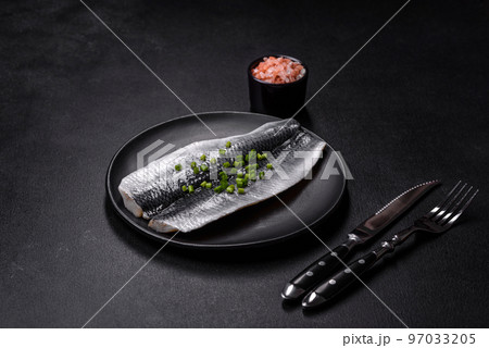 Marinated fillet with spices and herbs of sea herring on a black plate Marinated fillet with spices and herbs of sea herring on a black plate 97033205