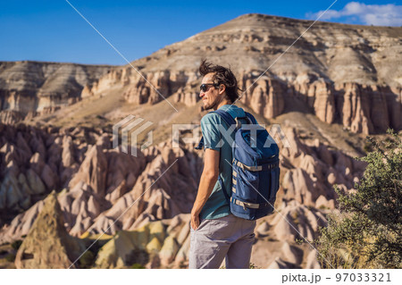 Young man exploring valley with rock formations and fairy caves near Goreme in Cappadocia Turkey Young man exploring valley with rock formations and fairy caves near Goreme in Cappadocia Turkey 97033321