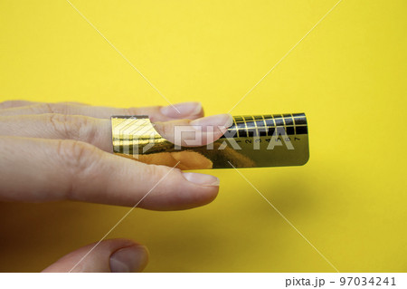Paper form for nail extensions on the client's nail. Master make nail extensions. Close-up of the fingers on a yellow background. 97034241