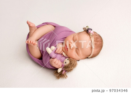 Sleeping newborn girl in the first days of life on a white background. A newborn baby in a purple lilac winding and a headband. Hand, palms of father and mother, parents hold the child. 97034346