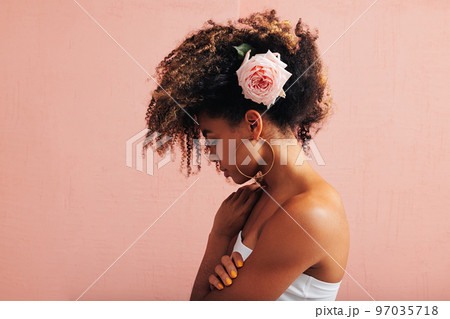 Side view of a young woman with pink flower in her curly hair	 97035718