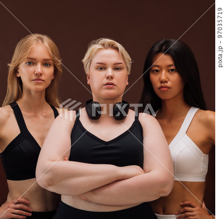 Three women with different body types standing together against brown background	 97035719