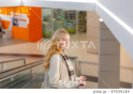 Young woman with long blond hair moving up on escalator 97036184