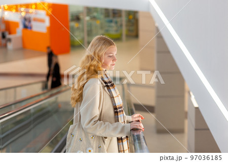 Young woman with long blond hair moving up on escalator Young woman with long blond hair moving up on escalator 97036185