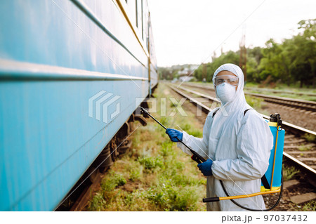 A man in a protective suit disinfects a train. Young man spraying disinfectant on public transportation. 97037432