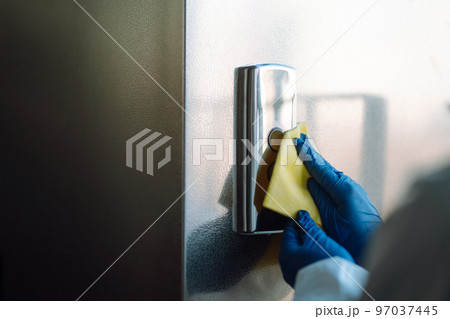 Cleaning and disinfection of the elevator to prevent COVID-19. Worker wearing protective suit sprays. Cleaning and disinfection of the elevator to prevent COVID-19. Worker wearing protective suit sprays. 97037445