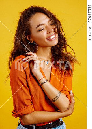 Portrait of young girl posing on yellow background. Pretty woman wears a carrot blouse and jeans. 97037557