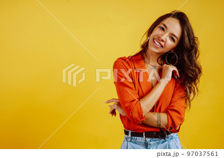 Portrait of young girl posing on yellow background. Pretty woman wears a carrot blouse and jeans. Portrait of young girl posing on yellow background. Pretty woman wears a carrot blouse and jeans. 97037561