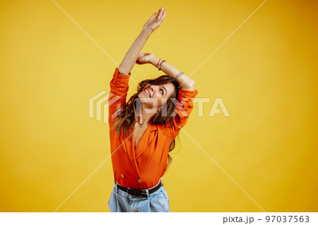 Portrait of young girl posing on yellow background. Pretty woman wears a carrot blouse and jeans. 97037563