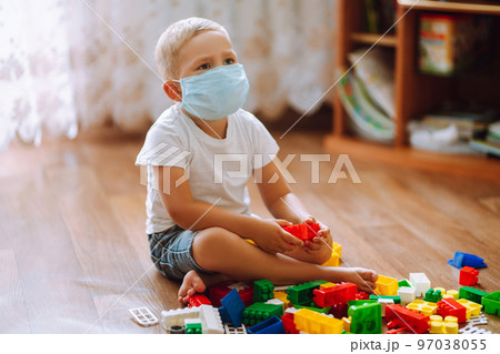 Concept of Covid-19 in quarantine city. Little child in medical mask. plays constructor. Concept of Covid-19 in quarantine city. Little child in medical mask. plays constructor. 97038055