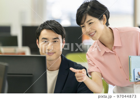 オフィスワーク　イメージ　PCのディスプレイを見て話す男女2人のビジネスパーソン 97044873