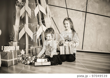 little sisters are looking at Christmas presents sitting in the modern living room. black and white photo little sisters are looking at Christmas presents sitting in the modern living room. black and white photo 97049539