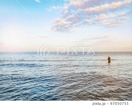 Fisher man stay in the water and pulling bait on his fishing rod. Baltic shore Fisher man stay in the water and pulling bait on his fishing rod. Baltic shore 97050755