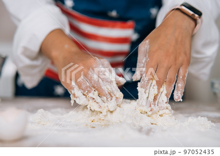 Young housewife in an apron kneads dough with her hands. Young housewife in an apron kneads dough with her hands. 97052435