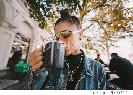 Cute young woman while drinking tea in modern street cafe Cute young woman while drinking tea in modern street cafe 97052579