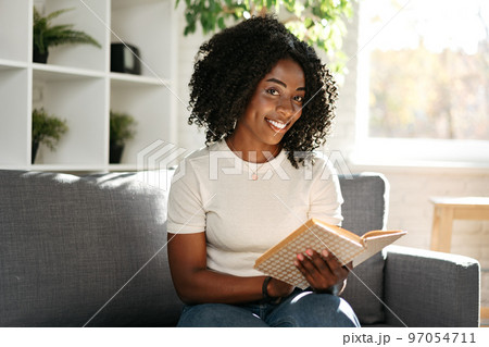 African woman reading book at home sitting on sofa African woman reading book at home sitting on sofa 97054711