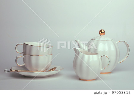 Beautiful white still life with white dishes for tea, coffee, with a golden spoon on a white background Beautiful white still life with white dishes for tea, coffee, with a golden spoon on a white background 97058312