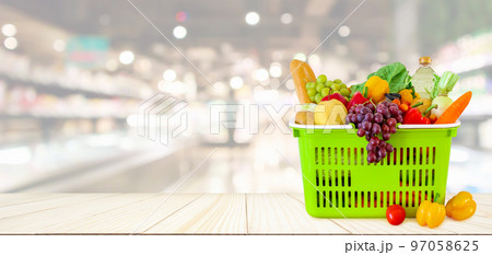 Shopping basket filled with fruits and vegetables on wood table with supermarket grocery store blurred defocused background with bokeh light 97058625